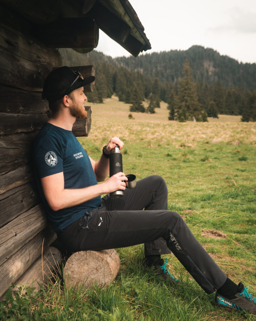 a man sitting on a log with a thermos, Konrad Płachta